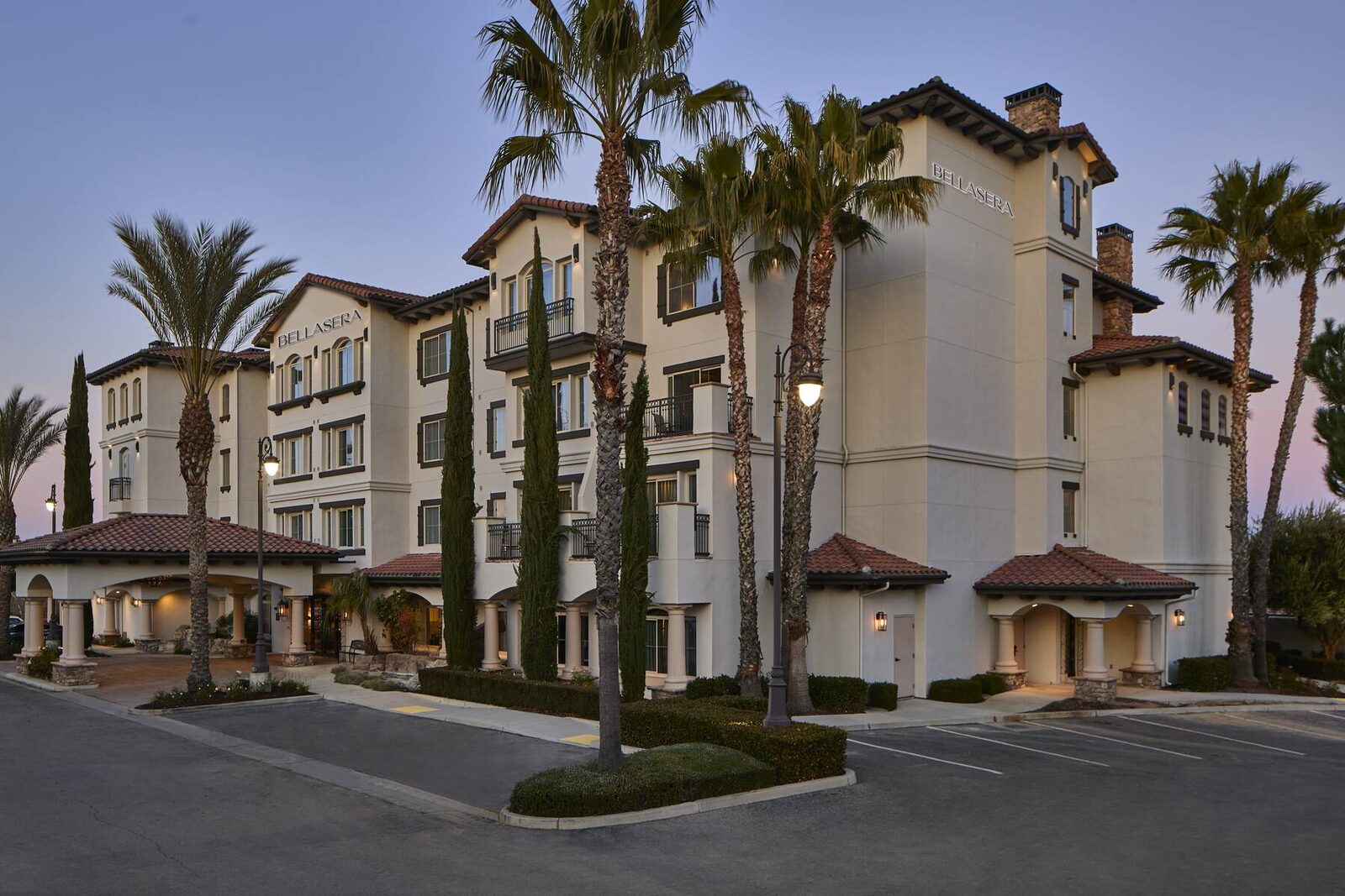 Bellasera Hotel & Suites exterior at dusk, framed by palms and cypress trees